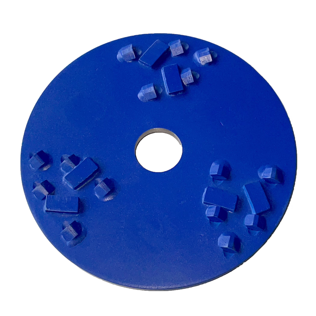 Derendinger_Dummy_Frästeller DS_REX_178859 Gros plan d'un disque abrasif circulaire bleu avec un trou de montage central. Le disque métallique peint en bleu présente plusieurs segments abrasifs rectangulaires et carrés en relief (diamant ou carbure) disposés sur sa surface ; certains segments montrent une légère usure et des résidus. La photographie montre la moitié supérieure du disque sur fond blanc, mettant en valeur la texture, la forme des segments et l'orifice central.