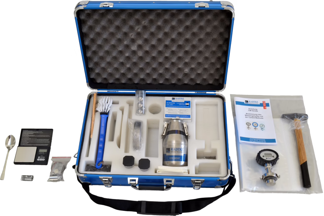 Open blue carrying case with foam inserts holding a moisture measurement kit. Visible items include a metal sample container labeled 'RADTKE MESSTECHNIK', a long-handled brush, a small digital scale with a spoon, a manual, a pressure/gauge instrument, a wooden-handled hammer, batteries, small sealed accessories and several black protective caps, all neatly arranged in cut foam compartments.