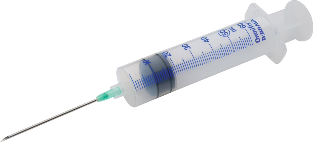 Pajarito_Dummy_Glue syringe_089417_ 089418_2021-02 Gros plan d'une seringue jetable en plastique avec une longue aiguille en acier inoxydable. Le corps transparent comporte des graduations bleues jusqu'à 60 ml et un joint en caoutchouc noir au piston ; le piston est partiellement enfoncé. L'aiguille est fixée par un embout en plastique vert et possède une pointe biseautée et affûtée. La seringue est posée sur un fond blanc uni et orientée en diagonale dans l'image.