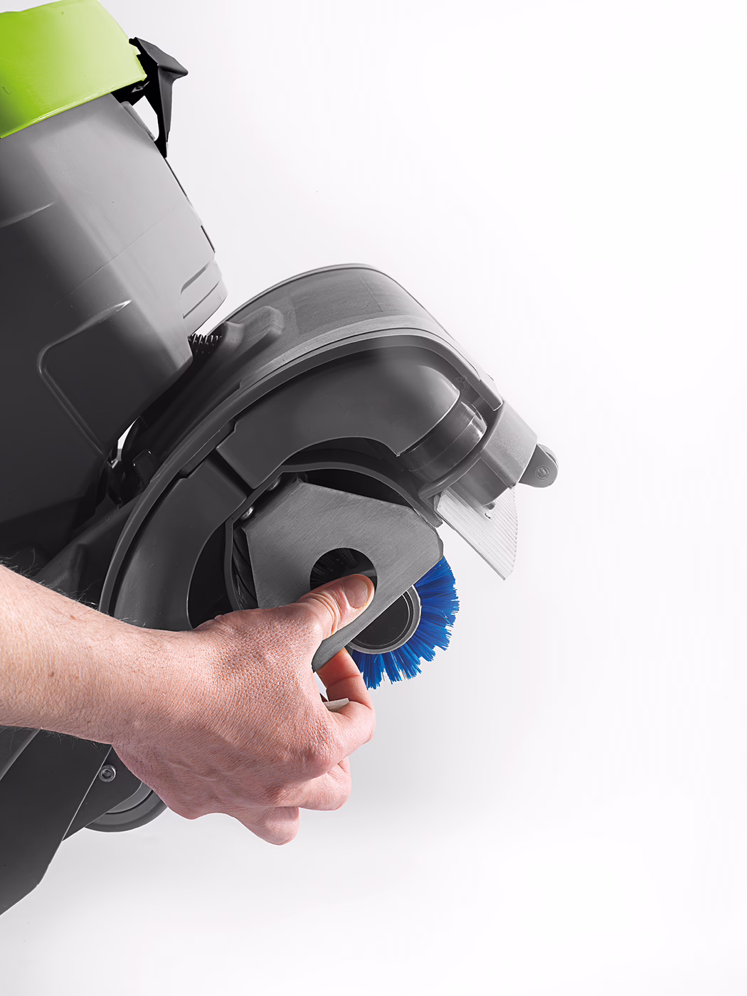 WOLFF_Product_detail_Cleanfox_Bürstenwechsel_2017 Gros plan sur une main tenant un module de brosse amovible d'un appareil de nettoyage de sol : boîtier en plastique gris, brosse circulaire bleue et capot vert citron visible au bord, fond blanc.