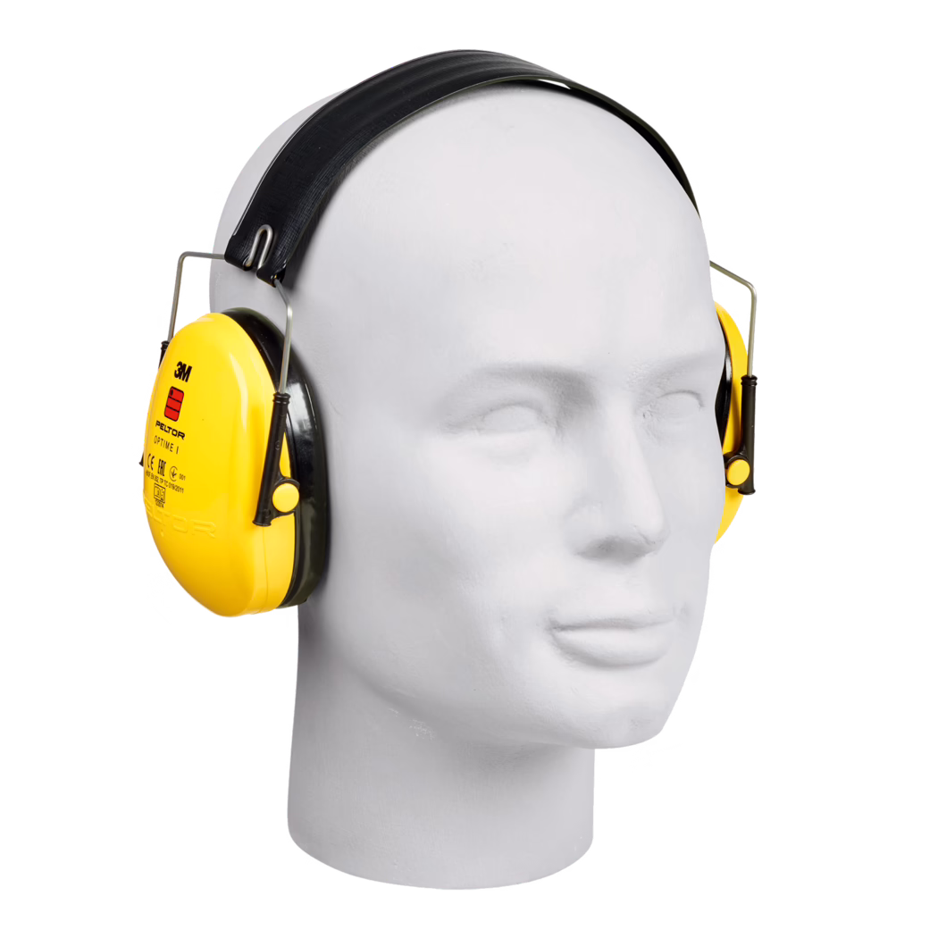 Close-up of a white mannequin head wearing bright yellow 3M Peltor Optime I over-ear hearing protectors. The image shows the upper half of the mannequin's face and head, centered, with a black textured headband, metal wire supports and glossy yellow ear cups bearing the 3M logo and product markings. Black foam-sealed cushions surround the cups and the cups are mounted on adjustable sliding metal arms. The background is plain white with soft, even lighting and minimal shadows, emphasizing the product's shape, material and vivid color. The photograph highlights the device as personal protective equipment for hearing protection in noisy industrial or construction environments.