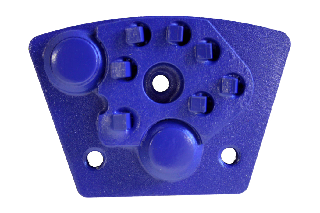 Gros plan d'un petit composant en plastique ou en métal de couleur bleue sur fond blanc. La plaque trapézoïdale présente deux saillies circulaires proéminentes, un trou circulaire central, plusieurs petits renforts carrés disposés près du haut et deux plus petits trous de fixation le long du bord inférieur. La surface est légèrement texturée et la couleur est d'un bleu cobalt vif.